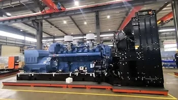 Un generador eléctrico industrial de gran tamaño, de color azul y negro, se muestra en el suelo de una fábrica con techo alto y grúas